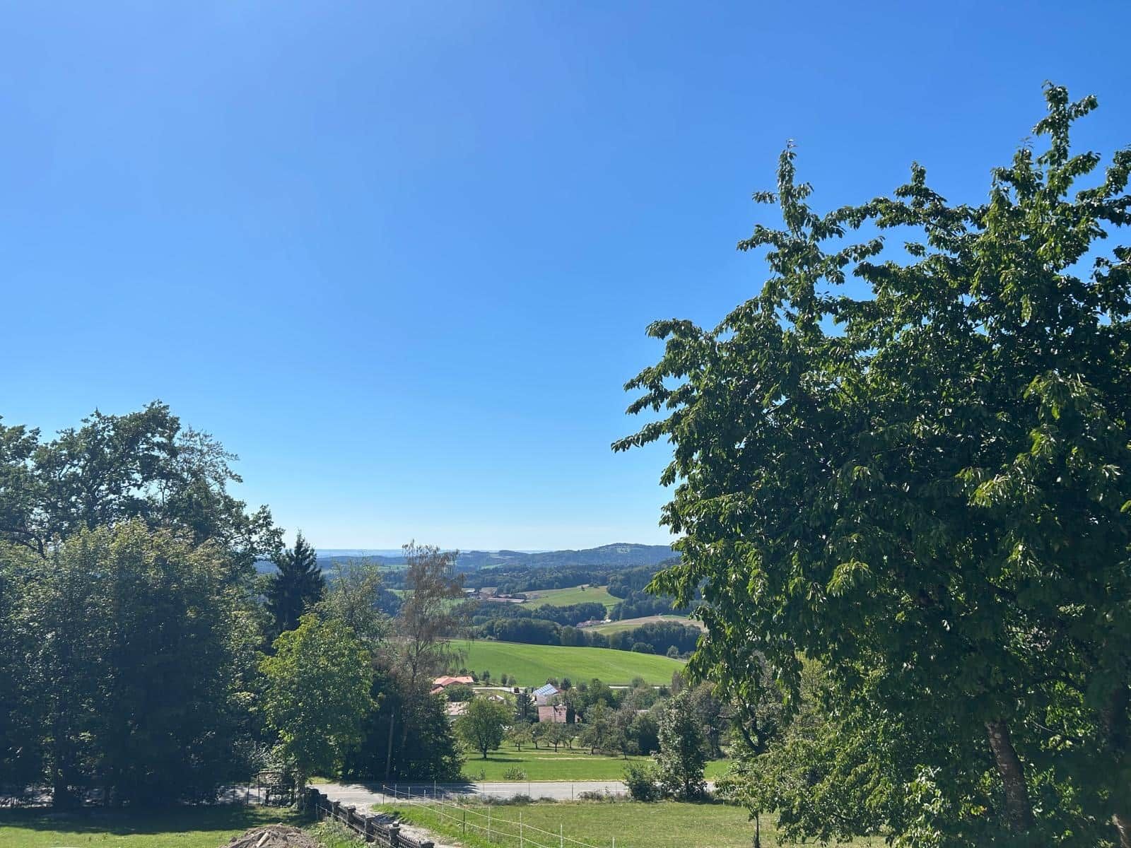 Un paysage rural caractérisé par un ciel dégagé, des champs verdoyants et un village situé au loin.