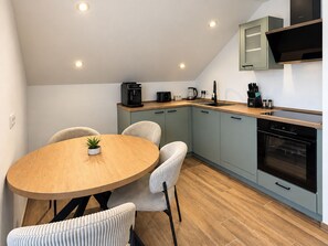 A modern kitchen with a round wooden table, light-colored chairs, and a built-in oven. - *NEW* Karl Vacation Rental with a magnificent view of the Bavarian Forest. (Lalling)