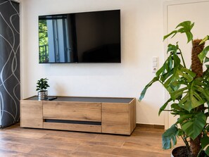 A modern living room with a flat-screen TV mounted on the wall, a wooden console table with drawers, and a large potted plant. - *NEW* Karl Vacation Rental with a magnificent view of the Bavarian Forest. (Lalling)