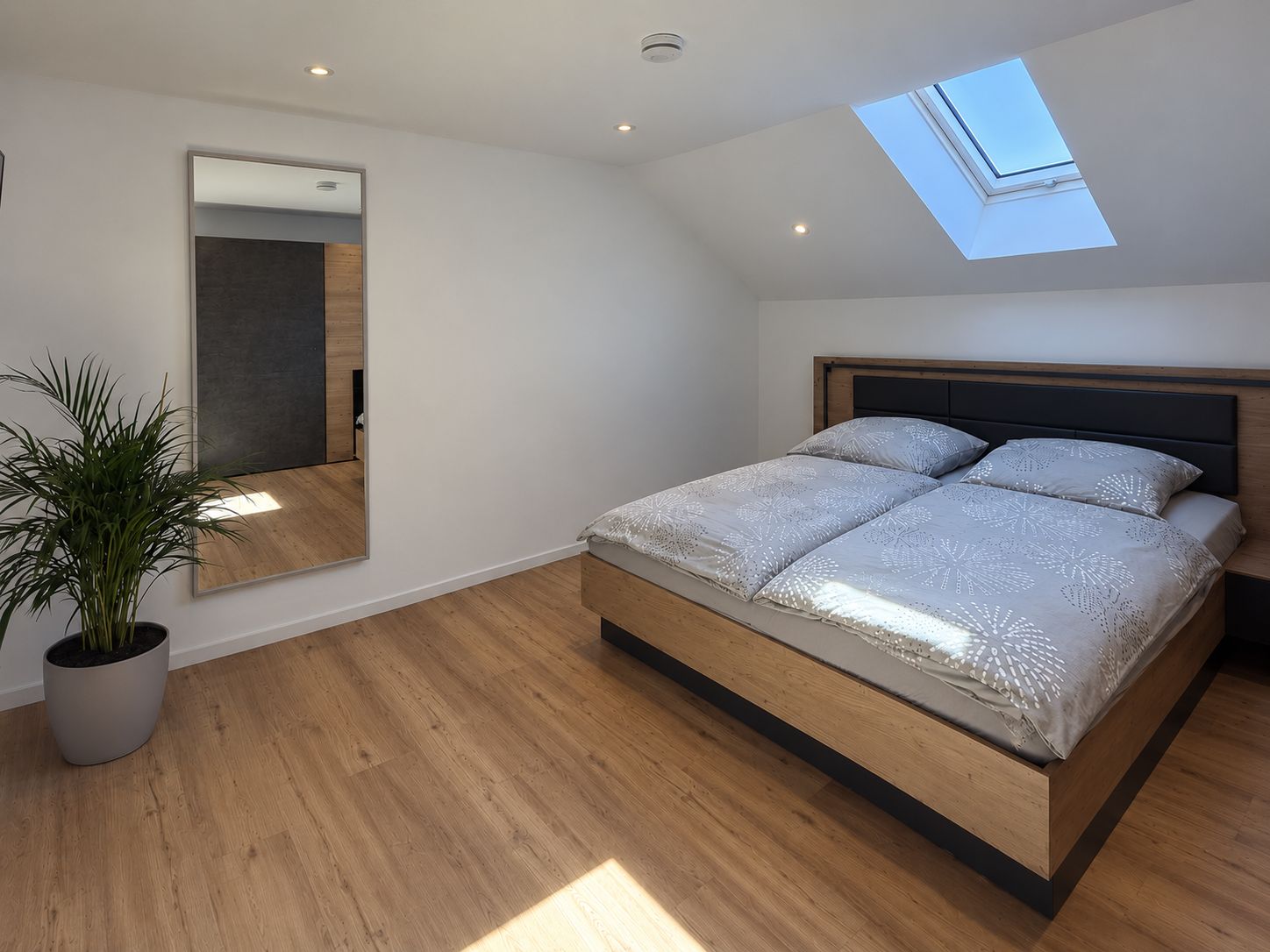 Un dormitorio moderno con tragaluces, una cama grande, una planta en maceta y un espejo.