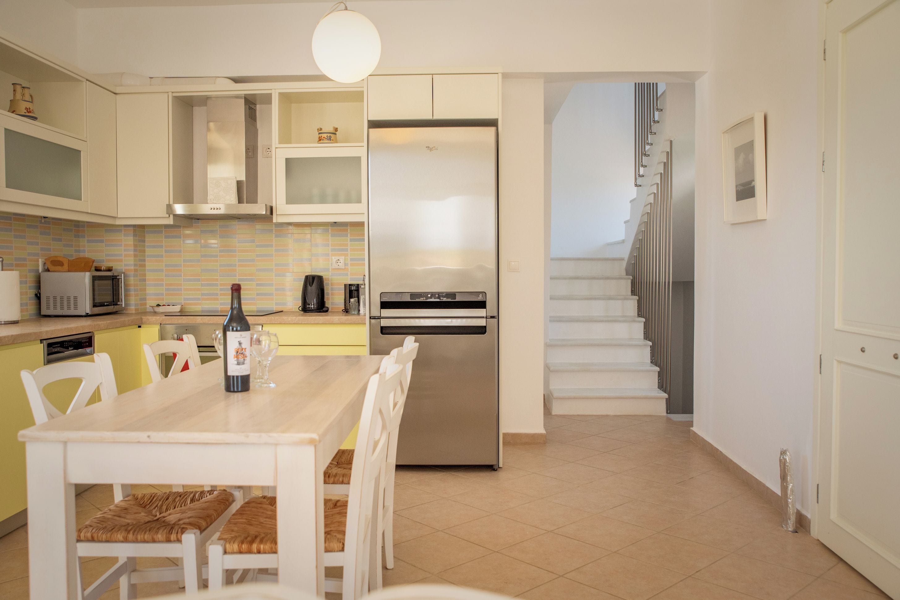 A modern kitchen with a built-in refrigerator, a dining table with chairs, and a staircase leading to an upper level.