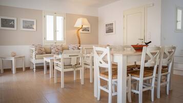 A dining area with a white table and chairs, a lamp, and a view of the sea through the window.