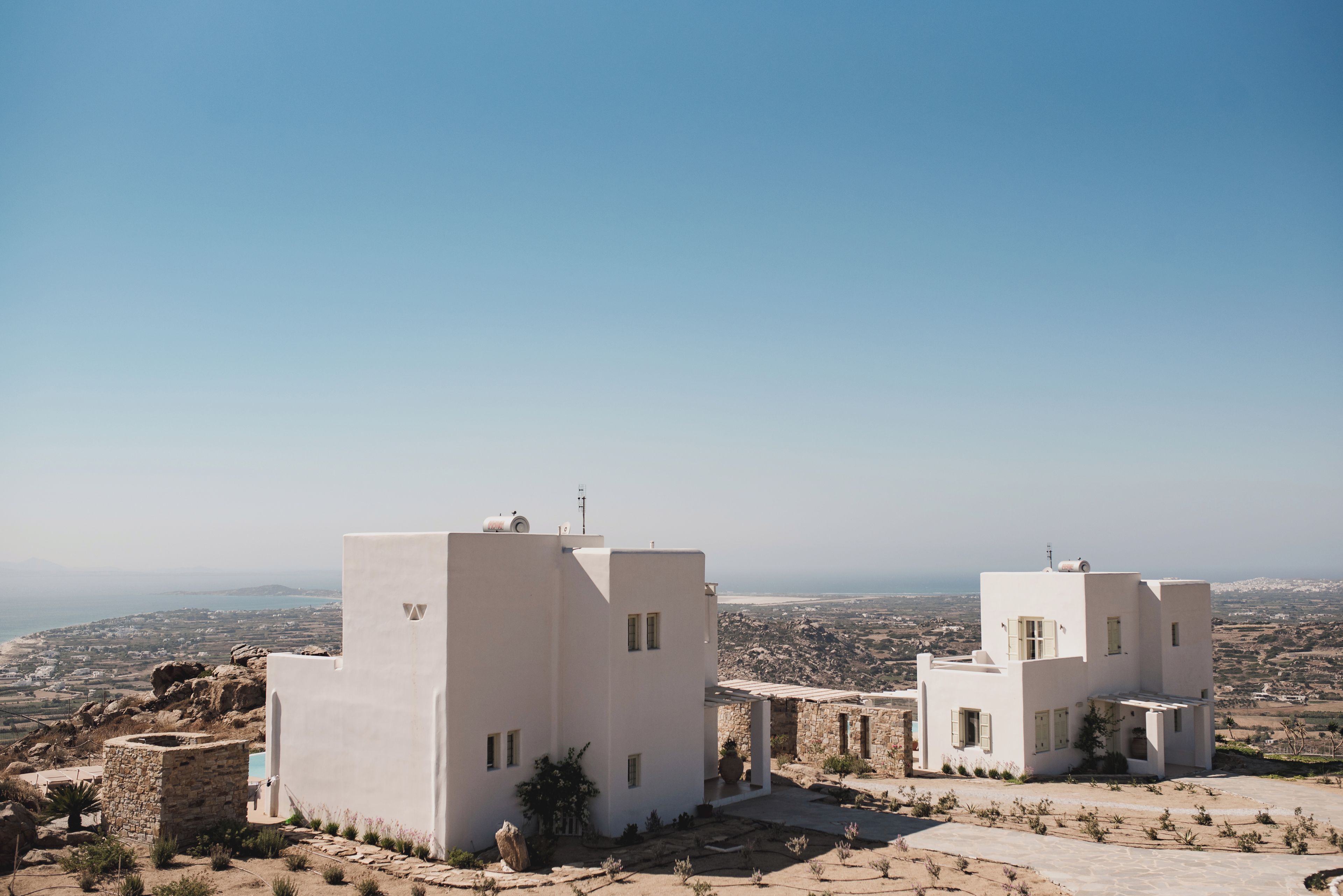 A white building with a stone structure in the foreground, set against a clear sky and a distant landscape.