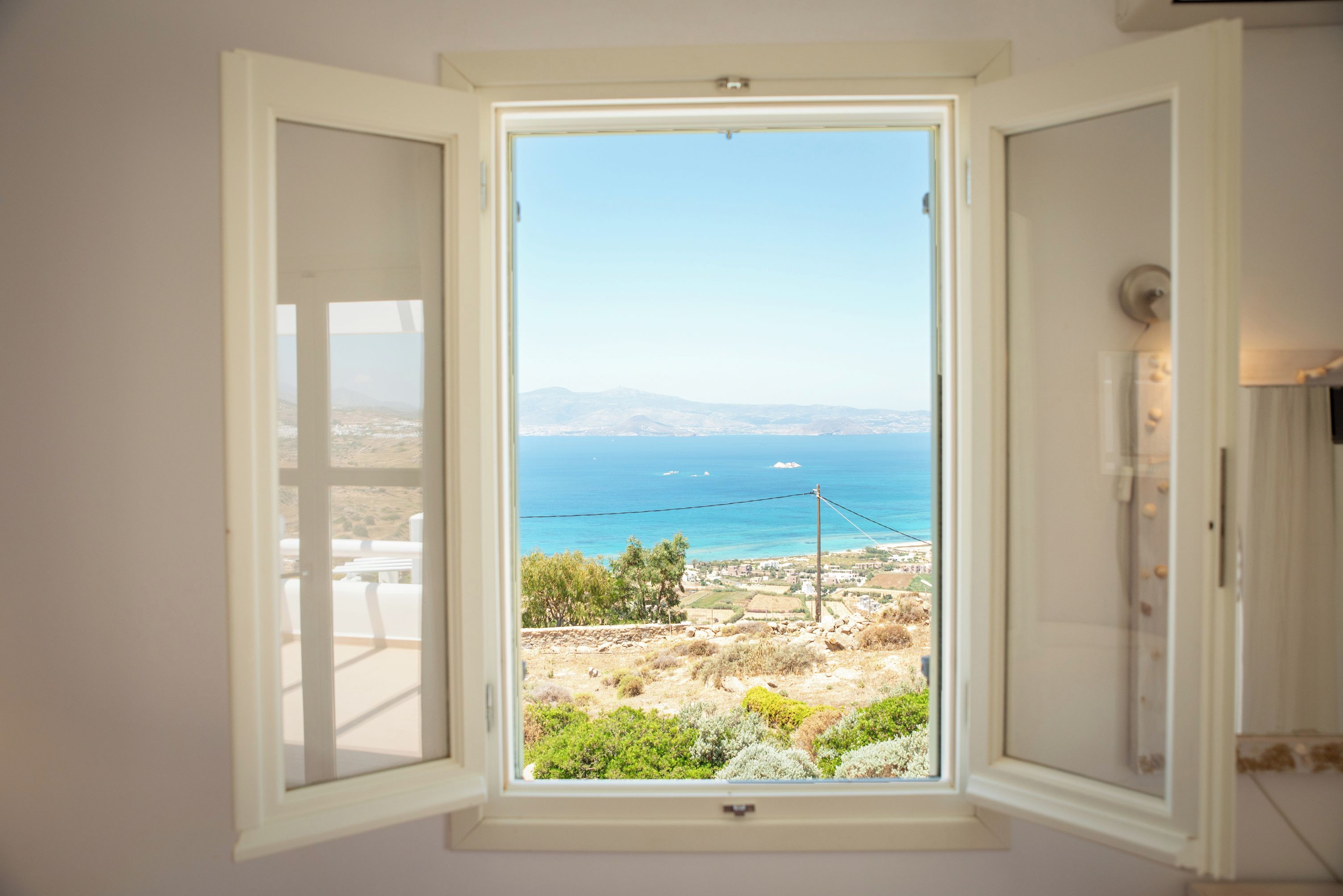 Una ventana con vista despejada al paisaje costero, incluyendo un cielo claro y montañas a lo lejos.
