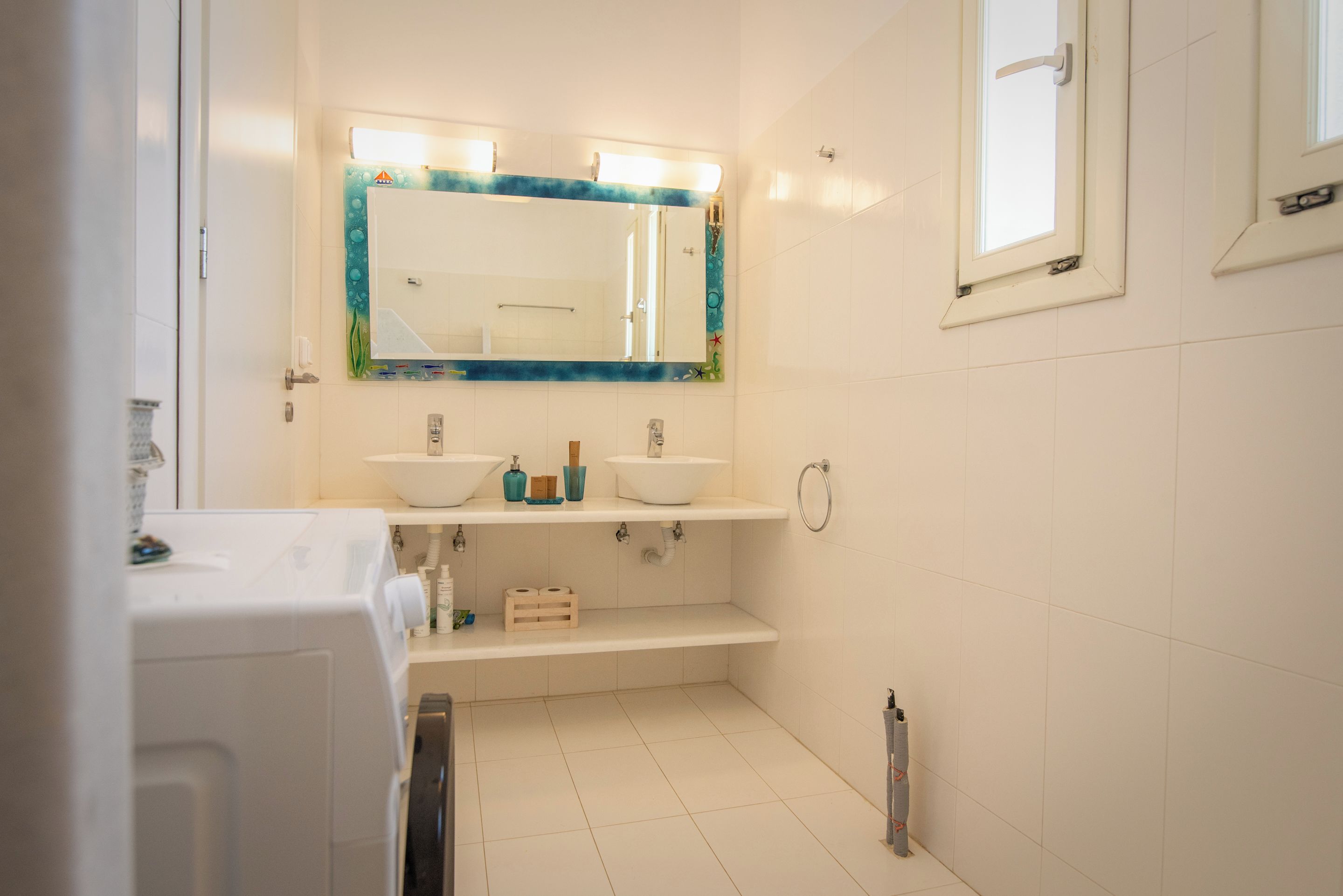 Un baño con dos lavamanos, un espejo con luces, un perchero para toallas y una ventana.