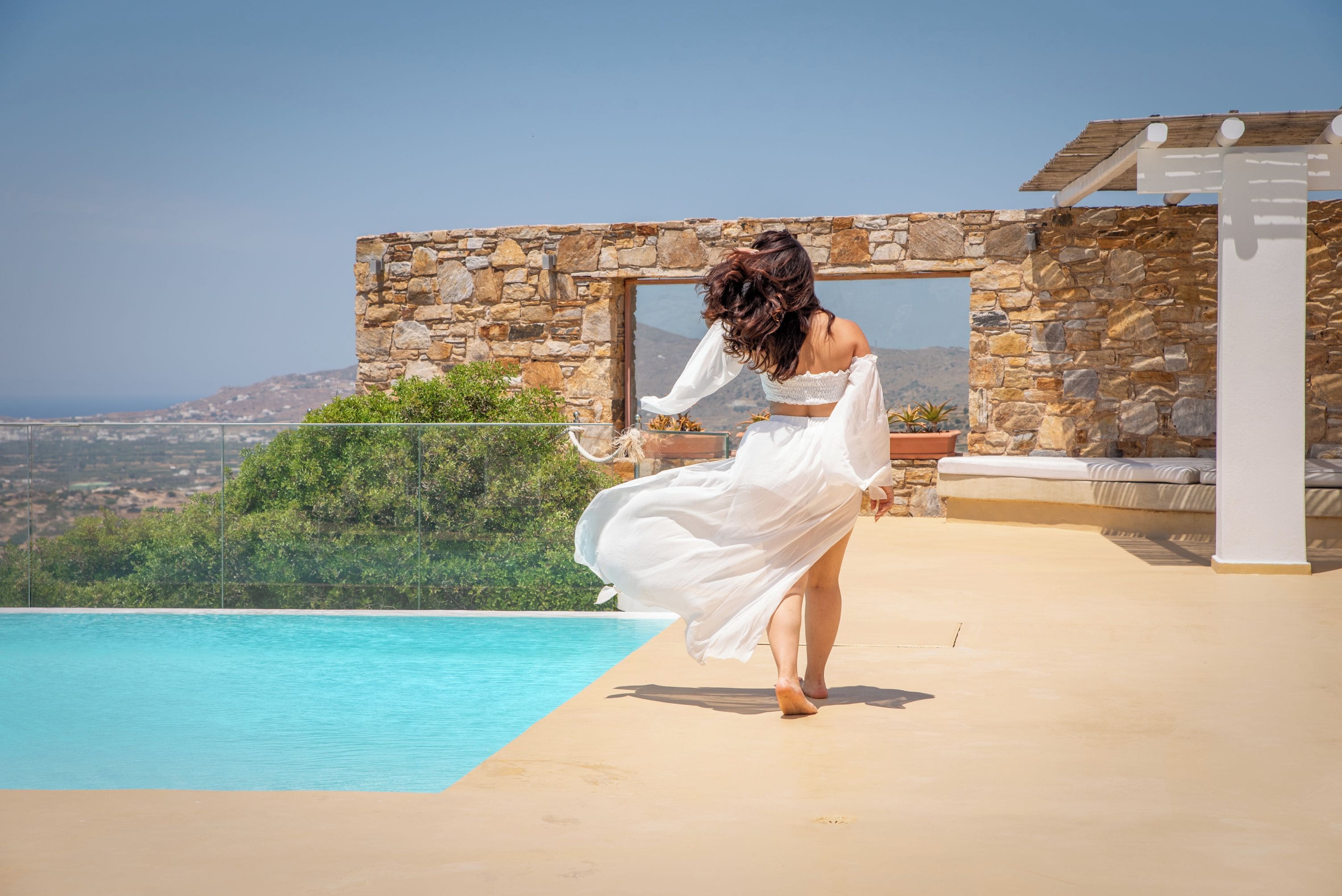 Una persona de pie junto a una piscina, con un edificio de piedra y vistas al paisaje.