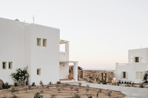 A white building with multiple windows and a stone wall in the background.