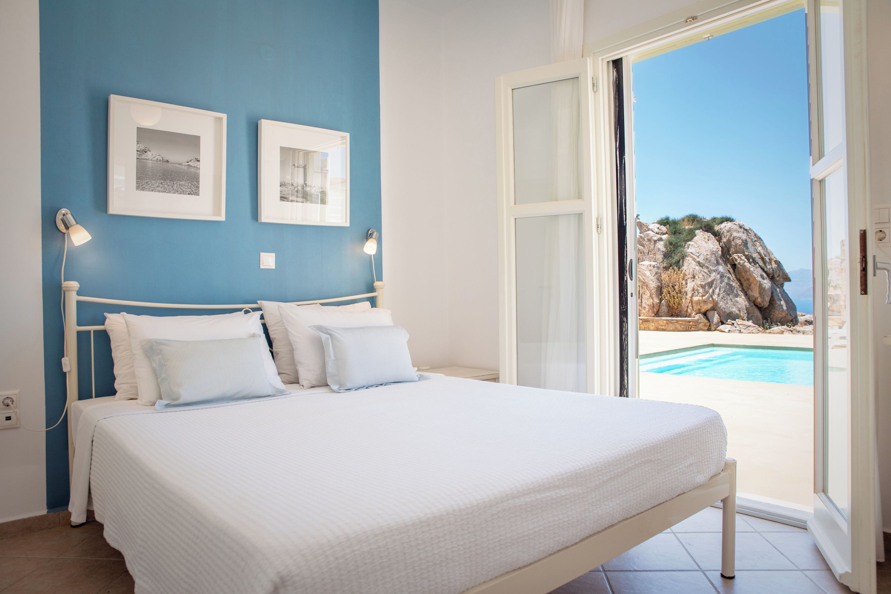 Une chambre à coucher avec un lit, deux lampes fixées au mur et une vue sur une piscine, visible à travers une porte ouverte.