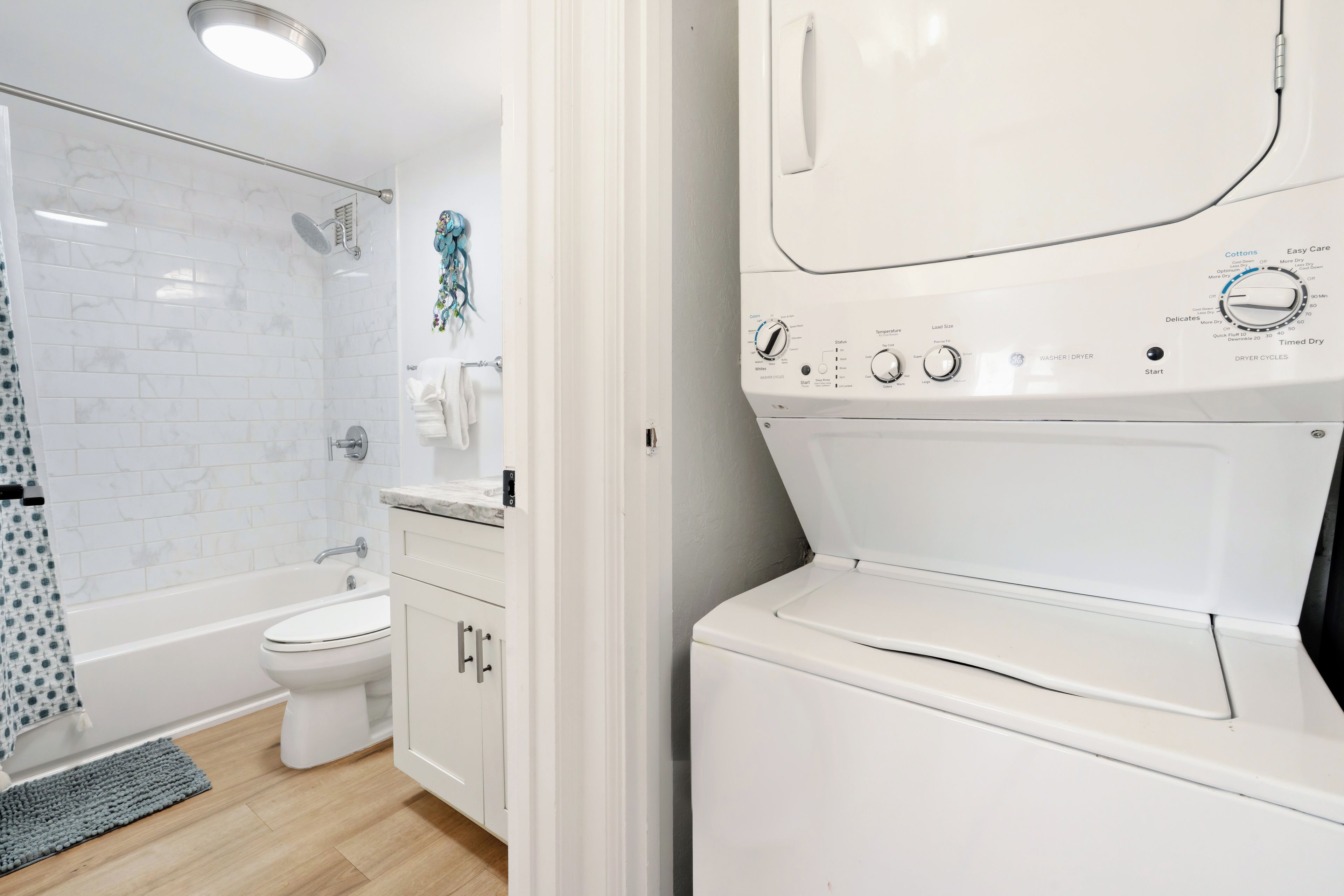 Un baño moderno con una bañera blanca, inodoro y una lavadora y secadora apiladas.