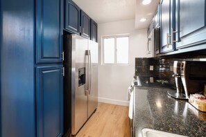 A kitchen with dark blue cabinets, a stainless steel refrigerator, a window, and a granite countertop. - Ocean-view 2BR/2BA Kihei condo with pool, AC, and beach access. (Kihei)