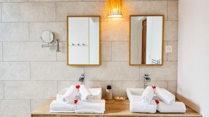 A bathroom with two sinks, each with a mirror above. There are towels on the sinks and a bottle of soap.