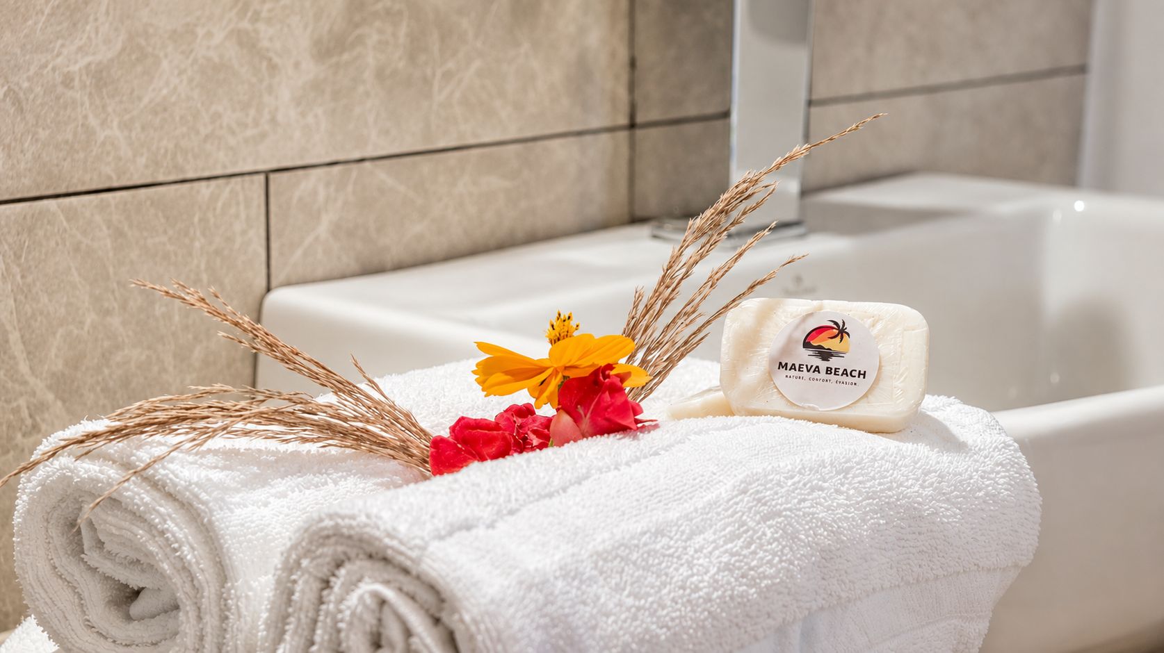 A neatly rolled white towel, a bar of soap, and decorative dried plants on a bathroom counter.