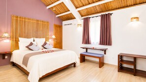 Une chambre à coucher comprenant un lit, des tables de chevet, un banc, une fenêtre avec des rideaux et un plafond avec des poutres en bois.