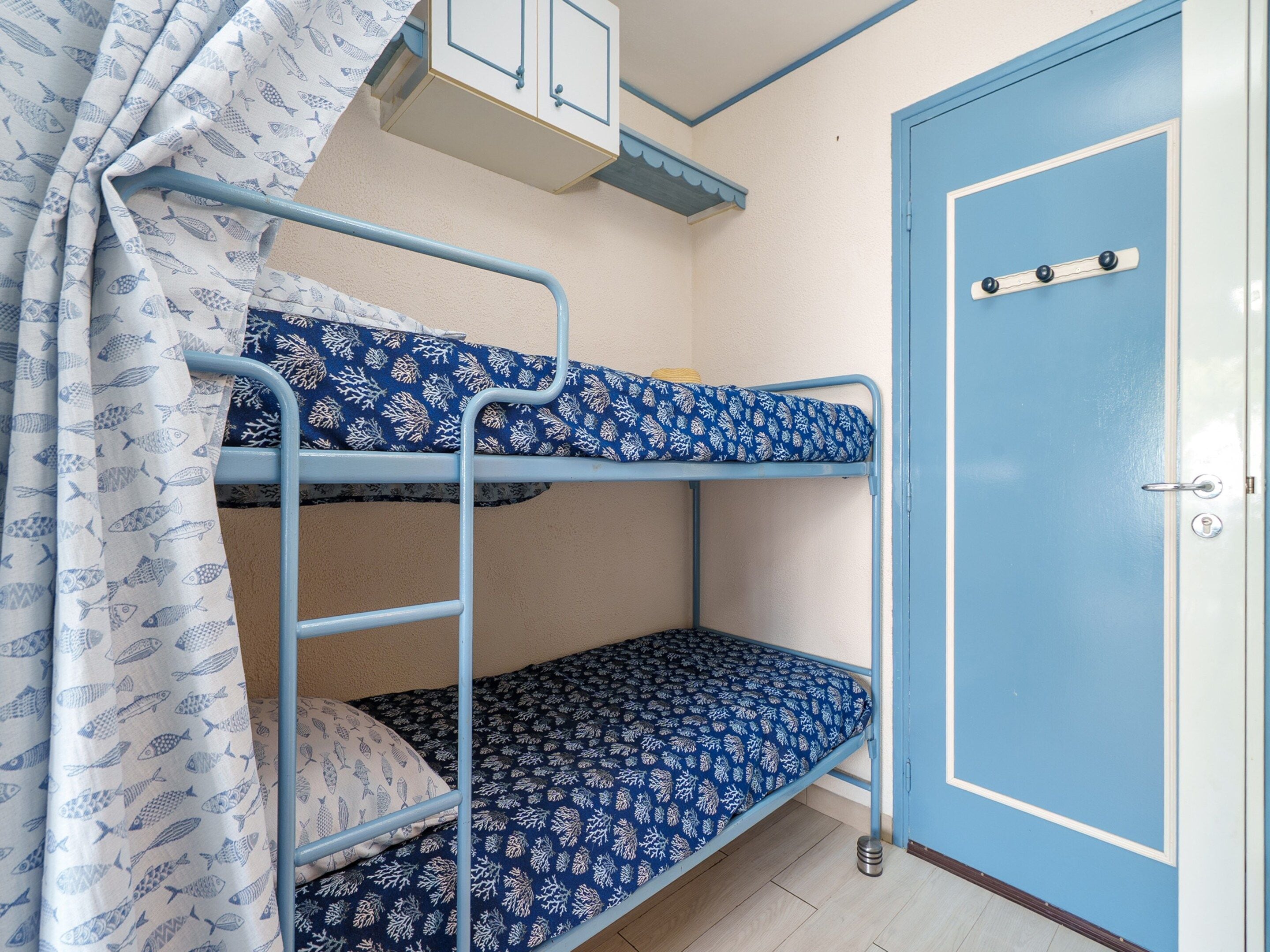 A bunk bed with patterned bedding, a door with a handle, and a small cabinet above the bed.
