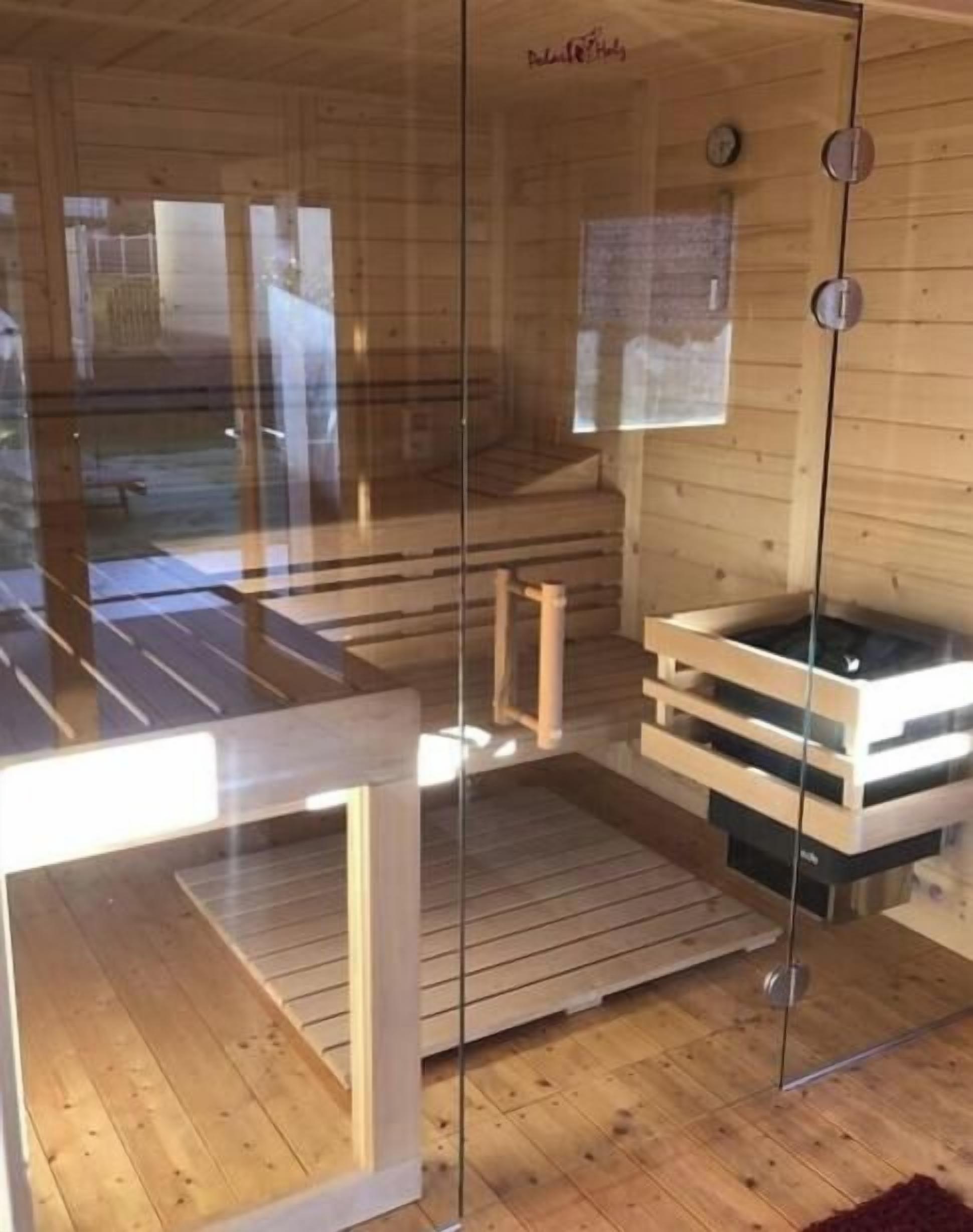 A sauna room with a glass enclosure, wooden benches, and a wooden floor.
