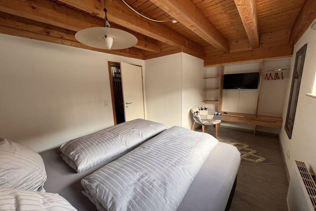 A bedroom with a bed, a chair, a TV, and a door.
