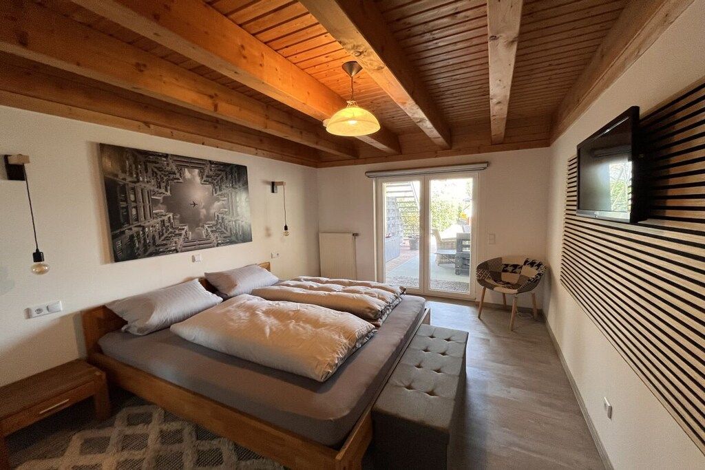 A bedroom with a bed, a bench, a wall-mounted TV, and a window.