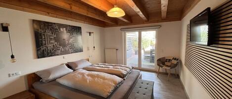 A bedroom with a bed, a bench, a wall-mounted TV, and a window.