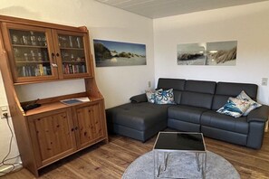 A living room with a sectional sofa, a wooden cabinet with glass doors, and two landscape paintings on the wall. - Shell apartment Country House Gertrude (Juist)