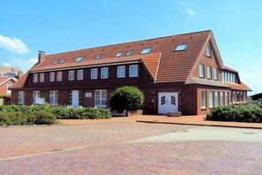 A two-story brick building with a pitched roof, multiple windows, and a paved driveway. - Shell apartment Country House Gertrude (Juist)