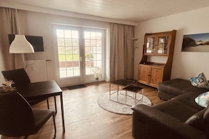 A living room with a sofa, a table, a lamp, and a cabinet. - Shell apartment Country House Gertrude (Juist)
