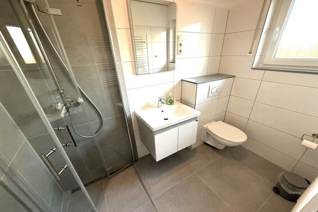 Un baño moderno con cabina de ducha de vidrio, un lavamanos blanco, un inodoro y un espejo sobre el lavamanos.