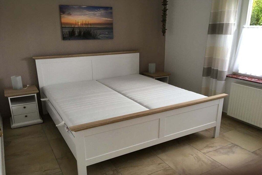 Une chambre à coucher avec un lit blanc, une tête de lit en bois, des tables de chevet et une fenêtre avec des rideaux.