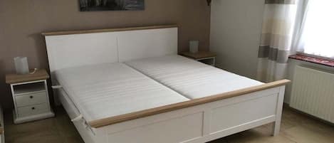 Quarto com cama branca, cabeceira de madeira, mesas de cabeceira e janela com cortinas.