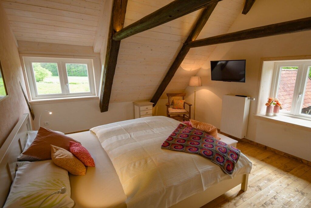 Ein Schlafzimmer mit Bett, Kissen, Fernseher, Stuhl und Fenster.