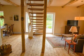 A wooden staircase leading to a door, a television on a cabinet, and a dining area with chairs and a table. - Holiday home Oertzeparadies (Hermannsburg\/Südheide)