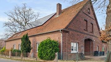 A brick building with a sloped roof, a chimney, and a large bush in front.