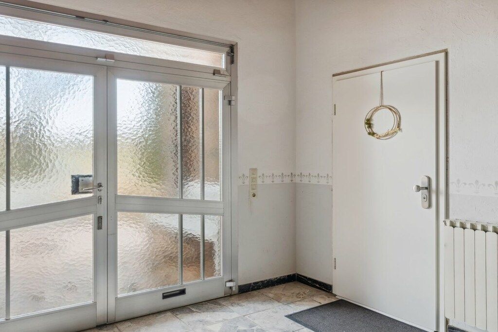 Ein Zimmer mit Glastür zum Außenbereich, einer weißen Tür mit Girlande und einem Heizkörper an der Wand.