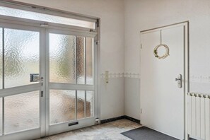 Ein Zimmer mit Glastür zum Außenbereich, einer weißen Tür mit Girlande und einem Heizkörper an der Wand.