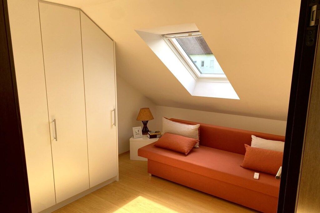 A room with a sloped ceiling, a skylight, a sofa, a nightstand, and a wardrobe.