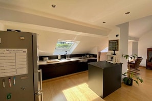 A modern kitchen with a built-in island, a skylight, and a refrigerator with a calendar. - JoMi holiday apartment (Mehring)