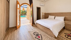 A bedroom with a wooden bed, a view of a swimming pool, and a door leading to an outdoor area. - 4-bedroom villa with private bathrooms, a pool, and air conditioning, near the airport (Essaouira)