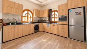 A modern kitchen with wooden cabinets, a stainless steel refrigerator, a washing machine, and a large window with a view. - 4-bedroom villa with private bathrooms, a pool, and air conditioning, near the airport (Essaouira)