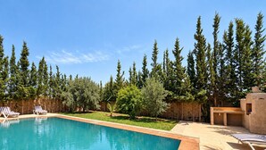 A rectangular swimming pool with a wooden deck surrounding it, a stone wall, and a barbecue area with a built-in oven. - 4-bedroom villa with private bathrooms, a pool, and air conditioning, near the airport (Essaouira)