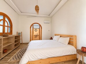 A bedroom with a wooden bed, a round mirror, a wooden desk, and a window with a wooden frame.