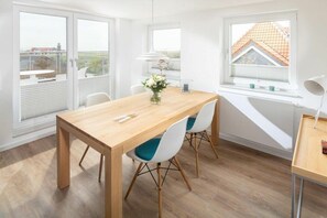 A dining area with a wooden table, white chairs, and a view through a window. - Holiday apartment in Juist with swimming pool (Juist)