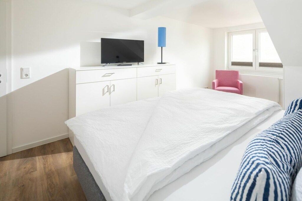 Ein Schlafzimmer mit einem Bett, einem Fernseher auf einer Kommode, einem Sessel und einem Fenster.