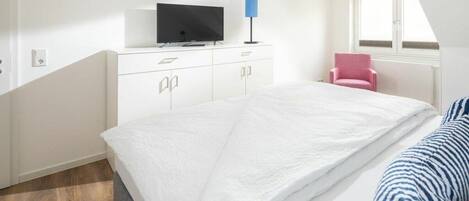 Une chambre à coucher avec un lit, un téléviseur posé sur une commode, une chaise et une fenêtre.