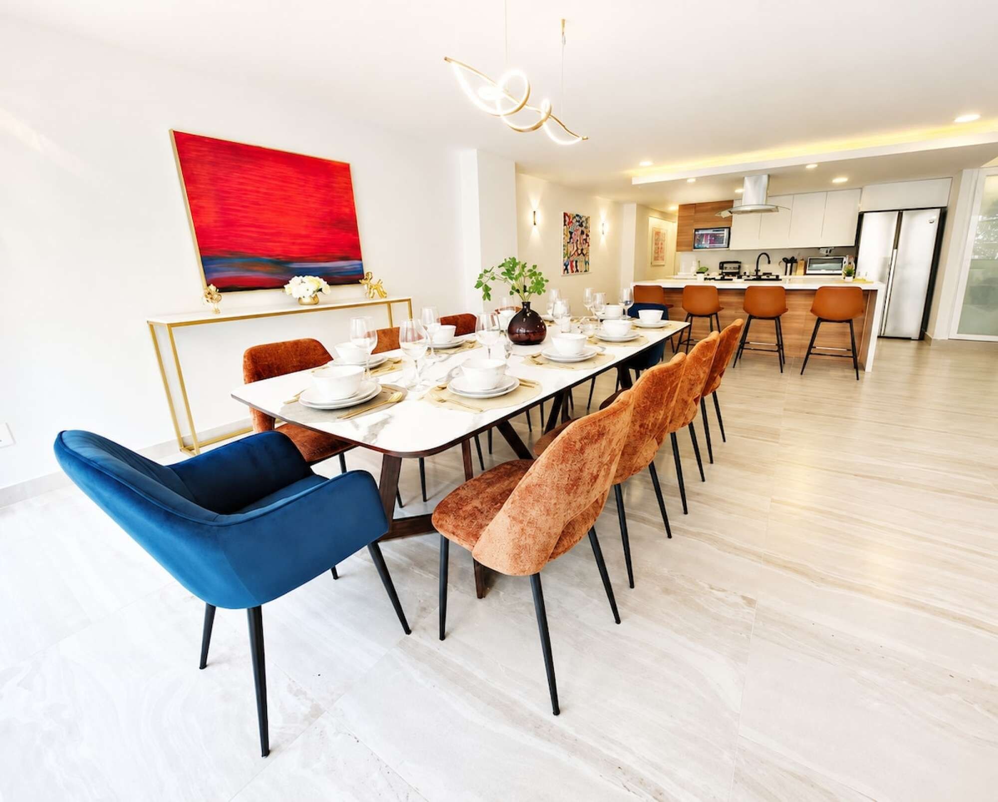 Uma sala de jantar moderna com uma mesa comprida posta para seis pessoas, rodeada por cadeiras de veludo em azul e castanho.