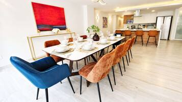 Uma sala de jantar moderna com uma mesa comprida posta para seis pessoas, rodeada por cadeiras de veludo em azul e castanho.