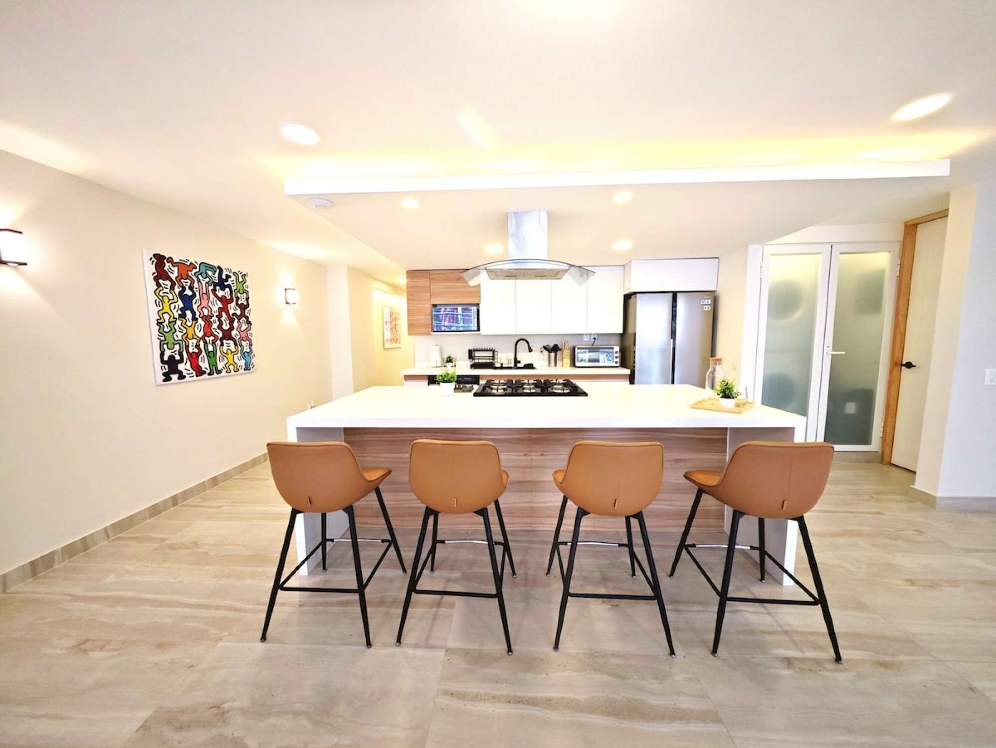 Cozinha moderna com ilha central, quatro banquetas de bar e uma pintura abstrata colorida na parede.