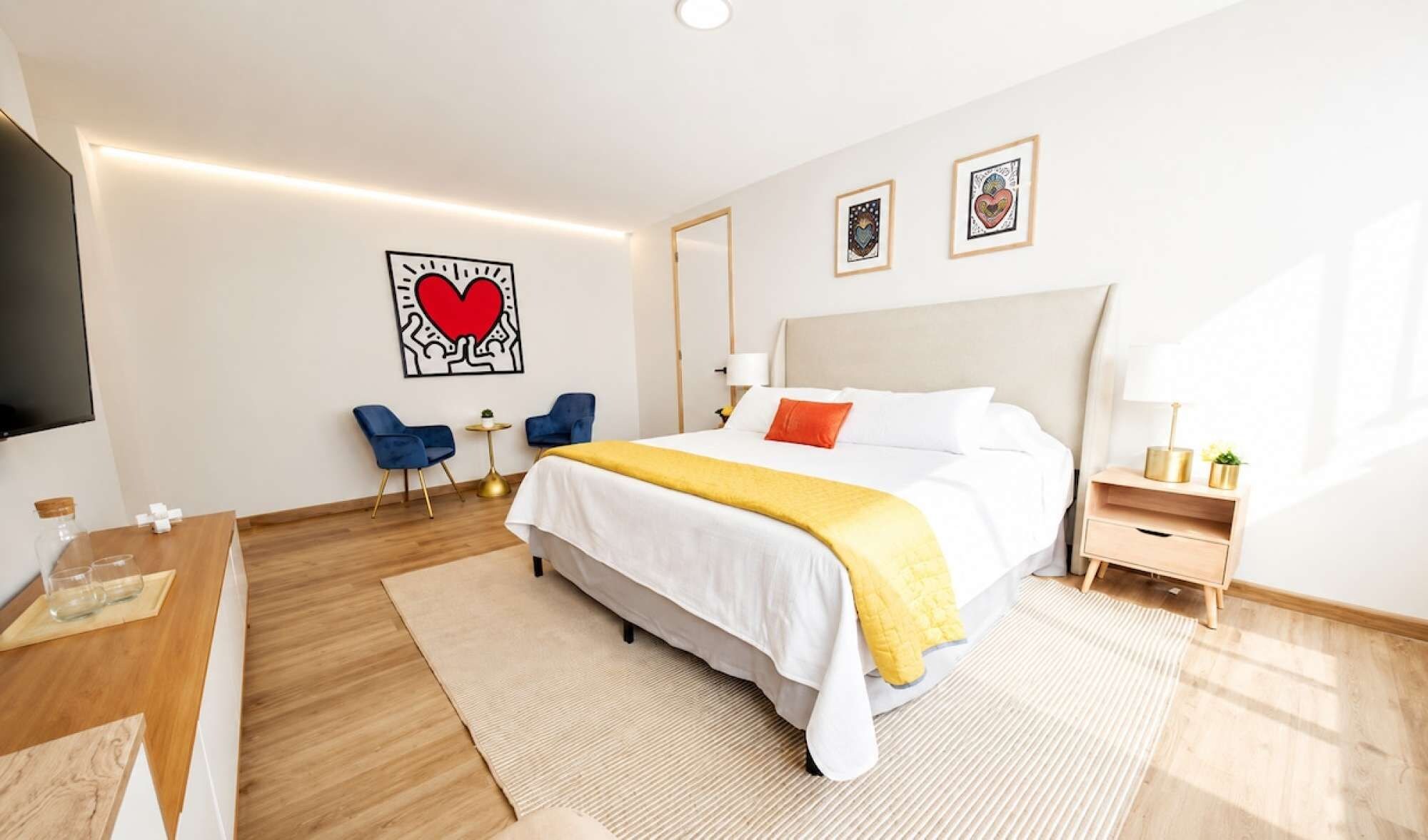 Et hotelværelse med seng, sengeborde, fjernsyn og kunst på væggene.