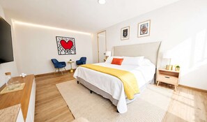 Una habitació d'hotel amb llit, taules de nit, televisió i obra d'art a les parets.
