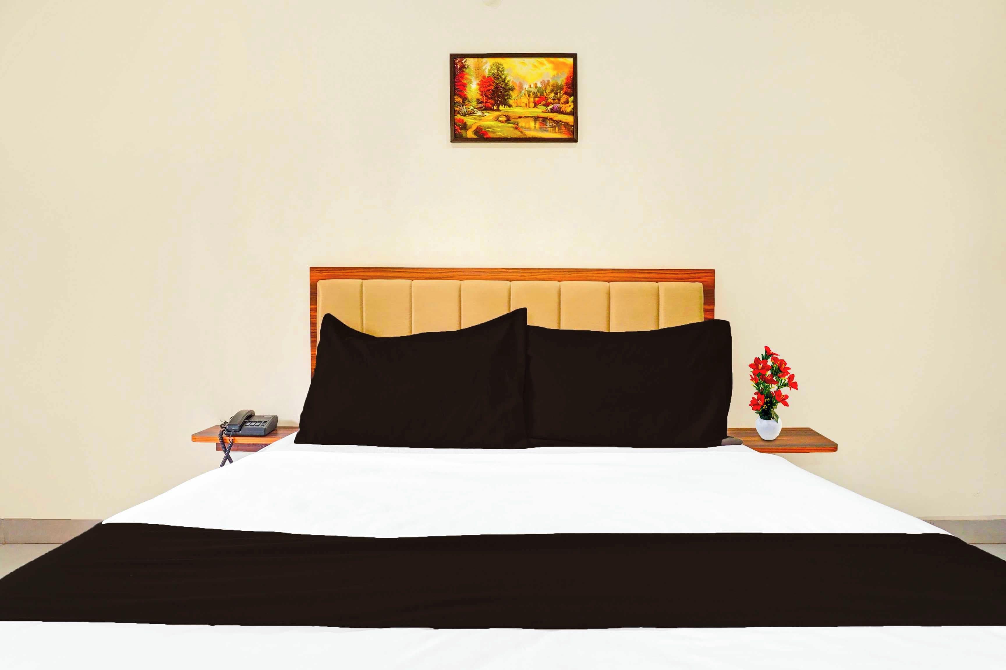 Una habitación de hotel con una cama, una mesita de noche, un teléfono y un cuadro en la pared.