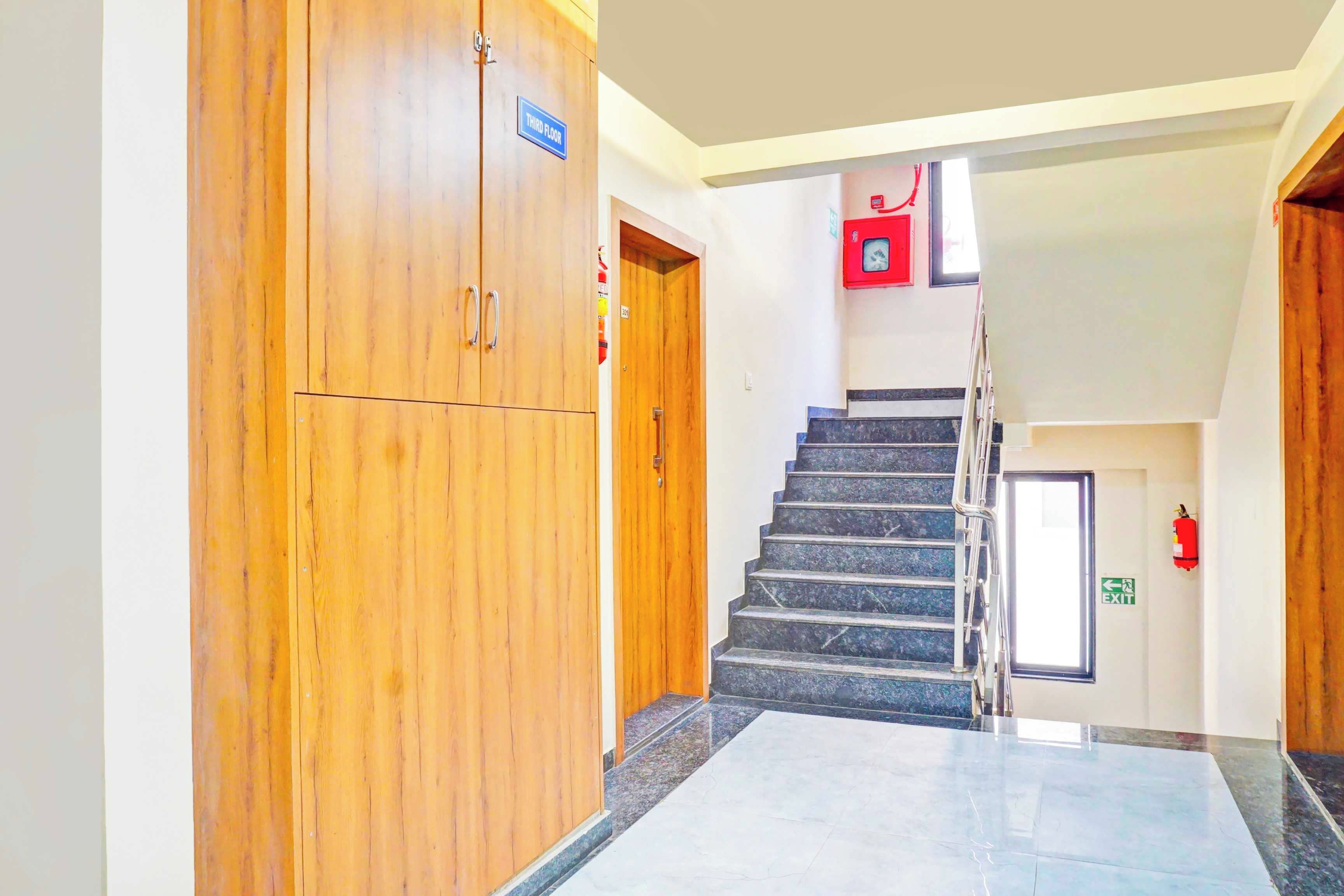 Un pasillo con una puerta de madera que indica 'Tercer Piso', una escalera con barandilla y un extintor en la pared.