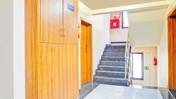 Un pasillo con una puerta de madera que indica 'Tercer Piso', una escalera con barandilla y un extintor en la pared.